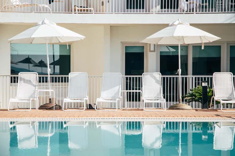 Poolside lounge area with white chairs, umbrellas, and reflecting water at modern resort