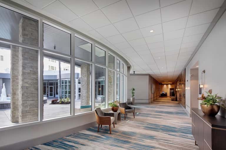Bright hotel corridor with large windows, stone columns, wooden flooring, and contemporary interior design