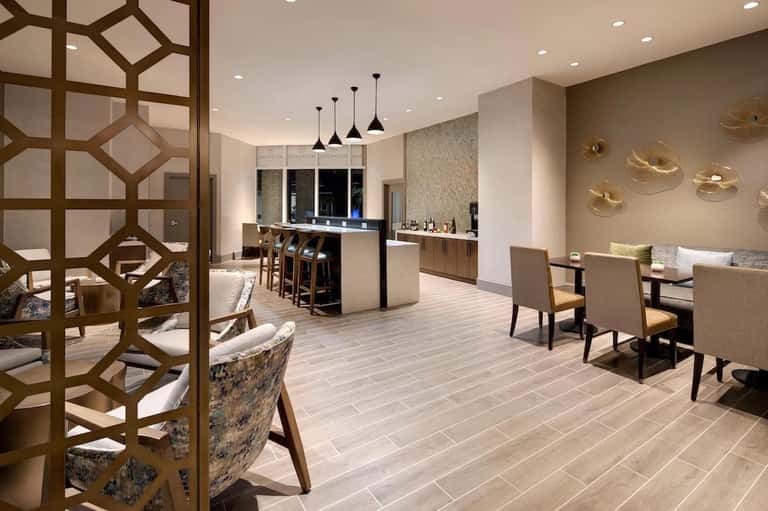 Contemporary hotel lounge with geometric wood screen, bar seating, pendant lights, and neutral decor