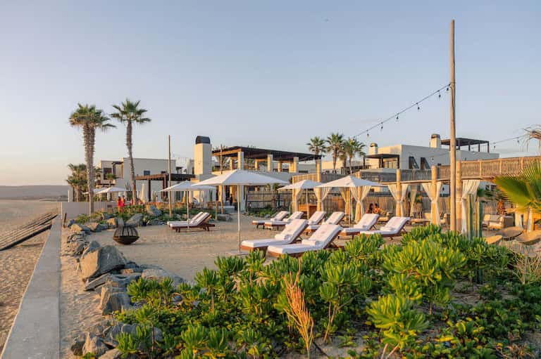 Beachfront resort with cabanas, lounge chairs, palm trees, and white sandy beach at sunset
