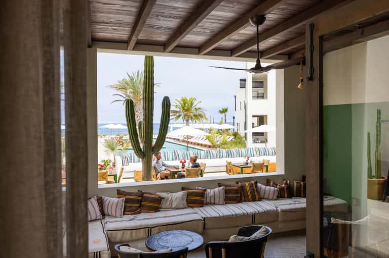 Modern lounge with window seat overlooking beach, cacti plants, and Mediterranean coastal view