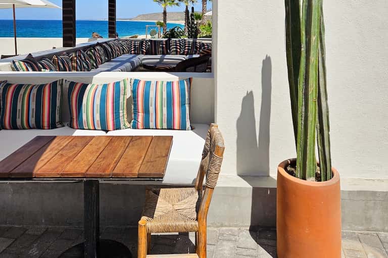 Beachfront lounge area with striped pillows on built-in seating overlooking ocean and blue sky