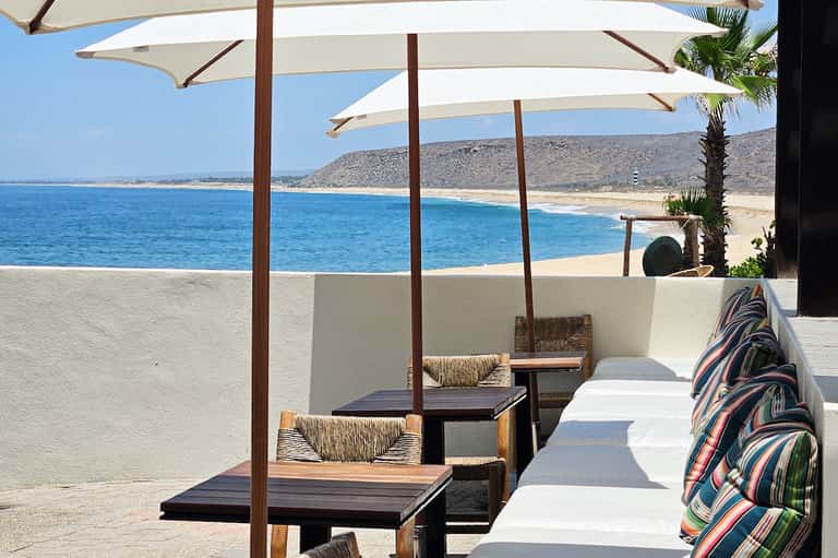 Beachfront lounge with white umbrellas, wooden platforms, and ocean views of sandy beach