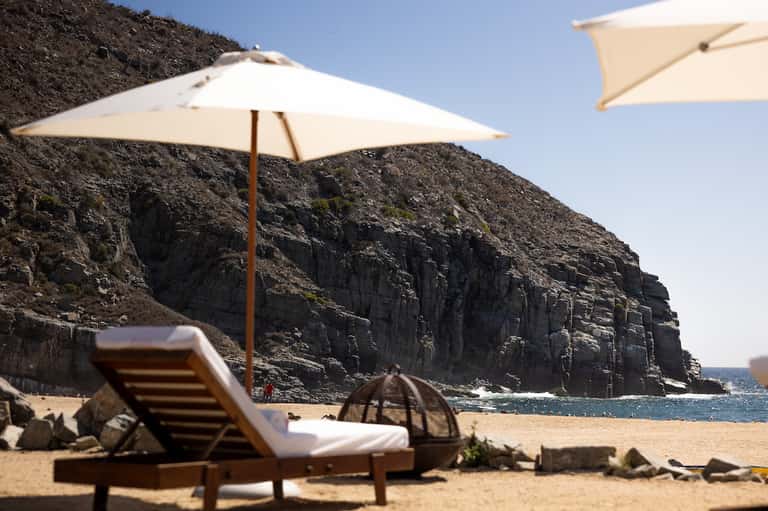 Beach lounge chairs and umbrellas positioned on sandy beach with dramatic black rock cliffs and ocean view