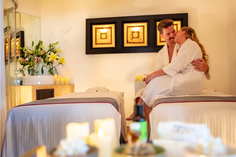Couple sitting on bed in hotel room with flower arrangement and framed artwork