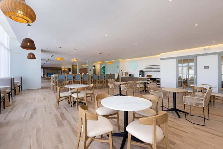 Contemporary dining area with wooden chairs, round white tables, and woven pendant lights