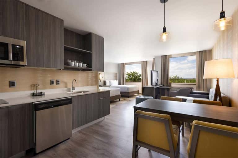 Upscale hotel suite with kitchenette, dining area, bedroom, and panoramic windows