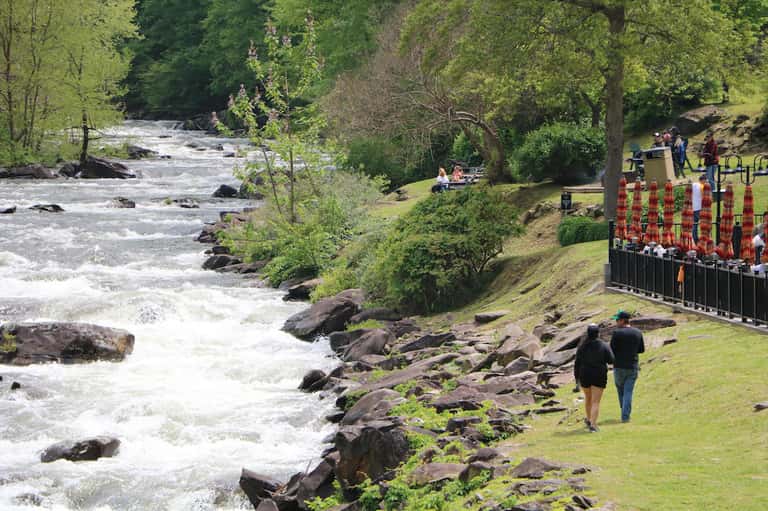 River landscape with rushing water, green trees, and visitors on grassy lawn
