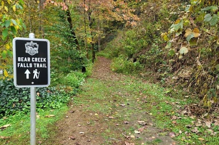 Bear Creek Falls Trail sign marking hiking path through lush green forest with autumn foliage