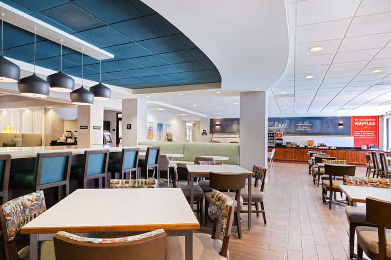 Modern hotel breakfast dining area with blue accent ceiling, pendant lights, and contemporary furniture