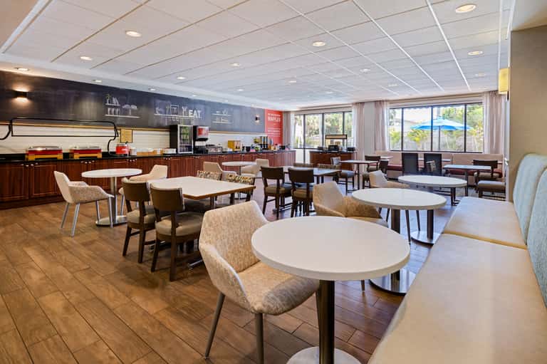Casual dining area with round tables, chairs, counter service, and windows with pool view