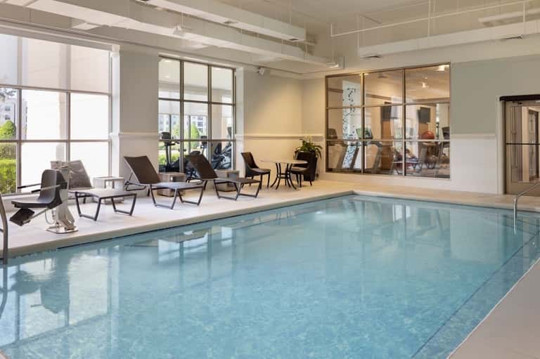 Indoor swimming pool with light blue water, lounging area, large windows, modern architecture