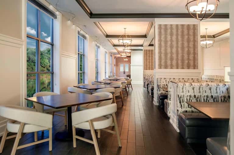 Elegant dining room with long tables, wooden chairs, pendant lights, and large windows overlooking greenery