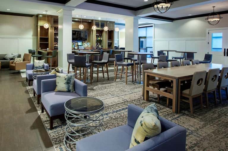 Upscale lounge with blue seating, bar area, wooden cabinetry, pendant lighting, and dining tables