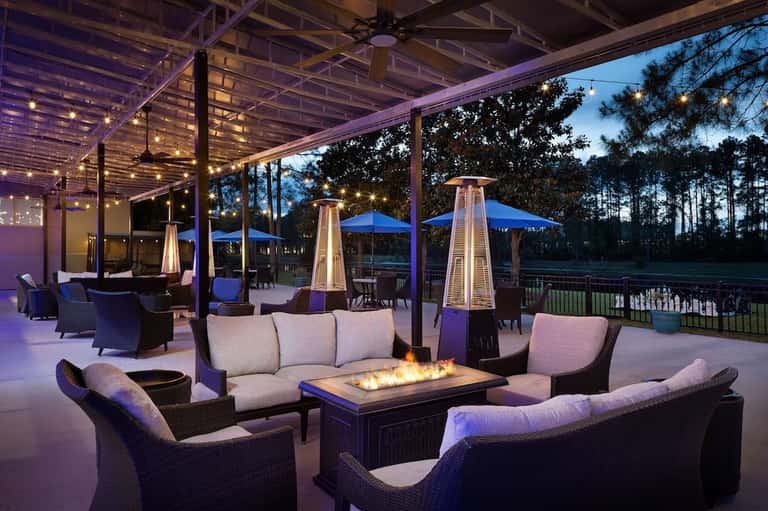 Elegant outdoor patio at dusk with fireplace, lounge seating, string lights, and blue umbrellas