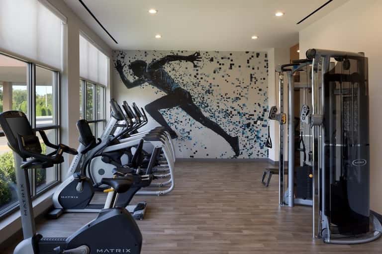 Modern hotel gym with cardboard cutout of athlete, Matrix exercise equipment, and large windows overlooking landscape