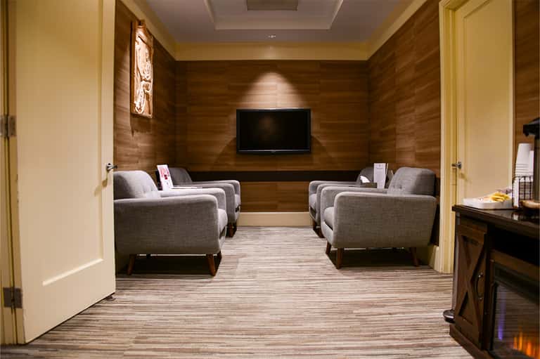 Private home theater with four gray upholstered armchairs facing a wall-mounted TV, warm wood paneling