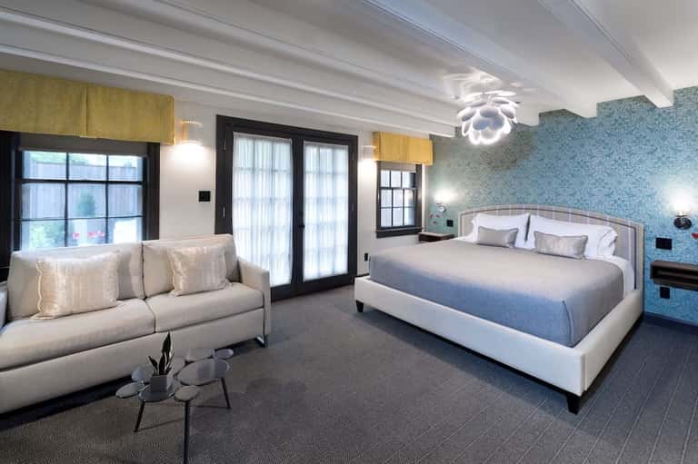 Luxury hotel suite with king bed, sitting area, blue patterned wallpaper, and modern lighting