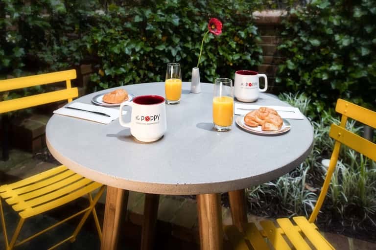 Outdoor breakfast table with yellow chairs, coffee, croissants, and fresh orange juice in garden setting