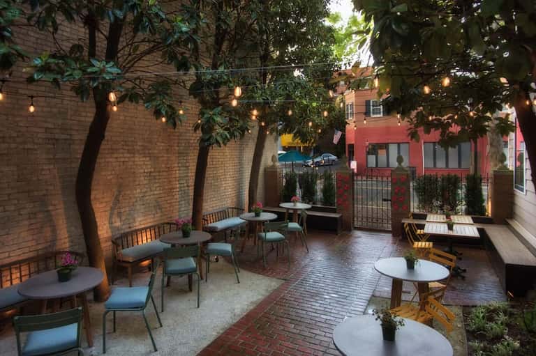 Intimate outdoor courtyard with brick walls, hanging lights, lounge seating, and climbing vines