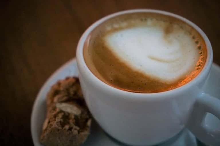 Latte with latte art in white cup and chocolate cookie on saucer