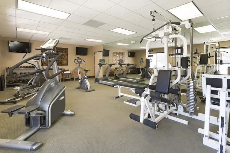 Fitness center with cardio equipment, weight machines, treadmills, ellipticals, and TV monitors on beige carpet