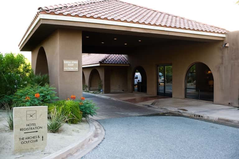 Tan stucco hotel entrance with arched doorways, clay tile roof, and desert landscaping at golf resort