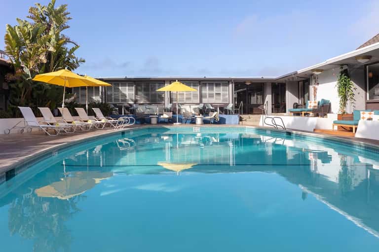 Luxury pool area with turquoise water, yellow umbrellas, lounge chairs, white building, and palm landscaping
