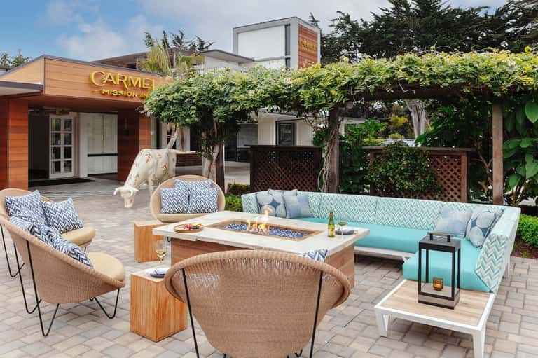 Outdoor patio with fire pit, turquoise sectional seating, woven chairs, and grapevine pergola at Carmel Mission Inn