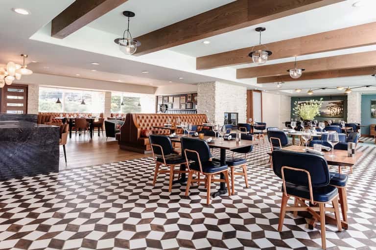 Upscale restaurant lounge with geometric floor, leather seating, wooden beams, and pendant lighting