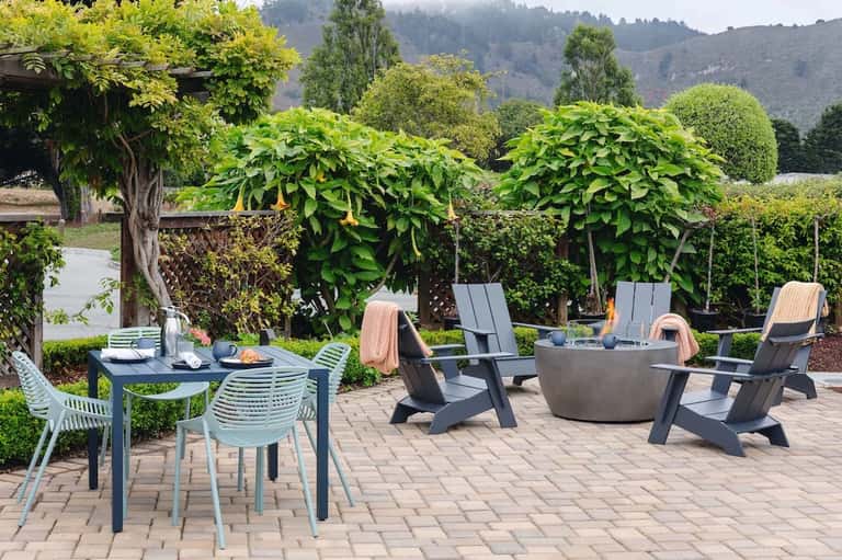 Outdoor patio with dining table, fire pit seating, and landscaped garden with mountain backdrop