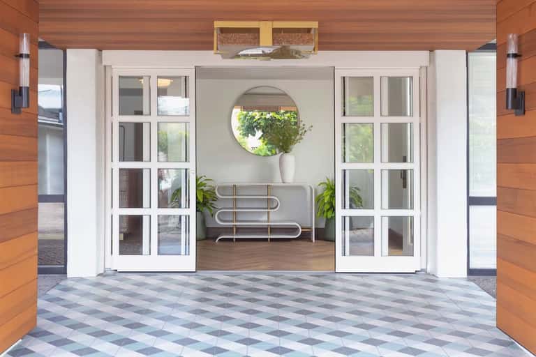 Elegant glass doors opening to a minimalist lounge with round mirror and potted plants