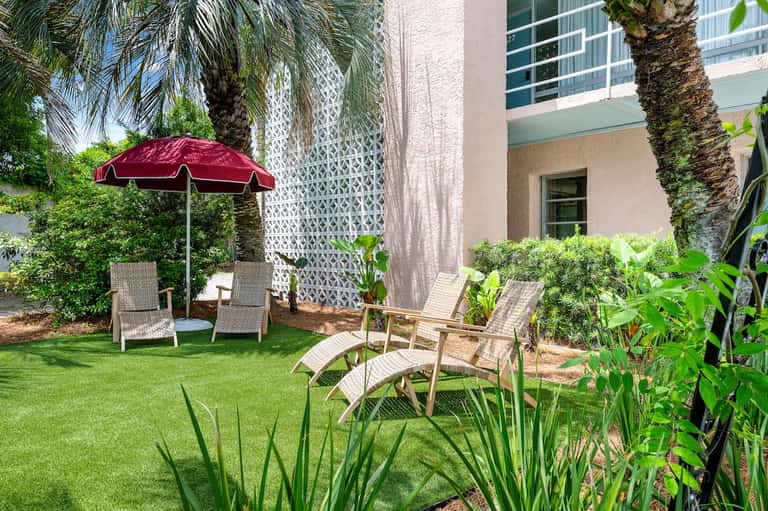 Resort courtyard with loungers, red umbrella, lush greenery, and tropical landscaping