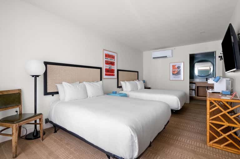 Hotel guest room with two queen beds, white bedding, and flat-screen TV on wall
