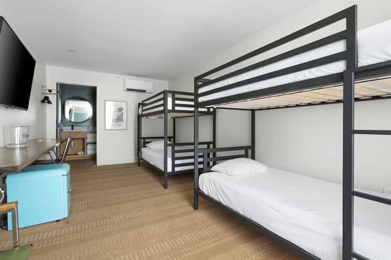 Modern dorm room with bunk beds, desk, TV, and bathroom