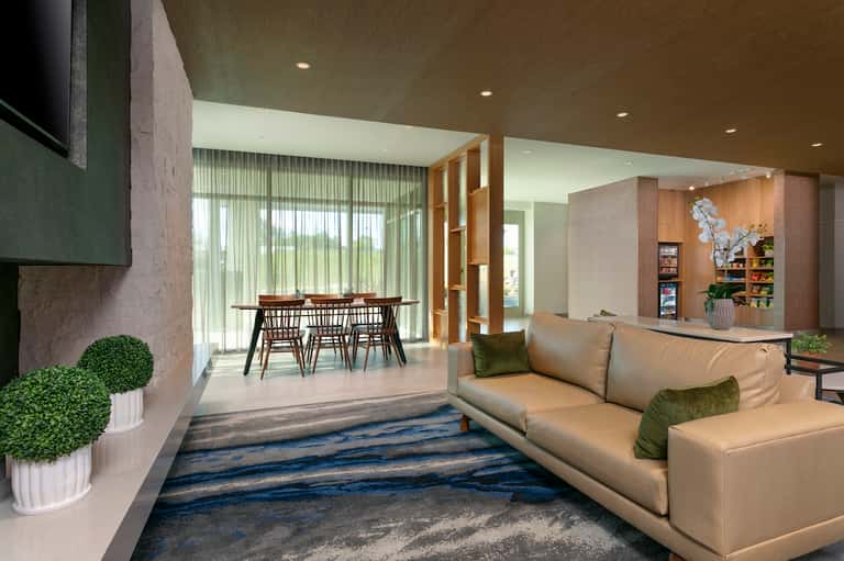 Modern hotel lobby with beige sofa, dining area, wooden accents, and contemporary design