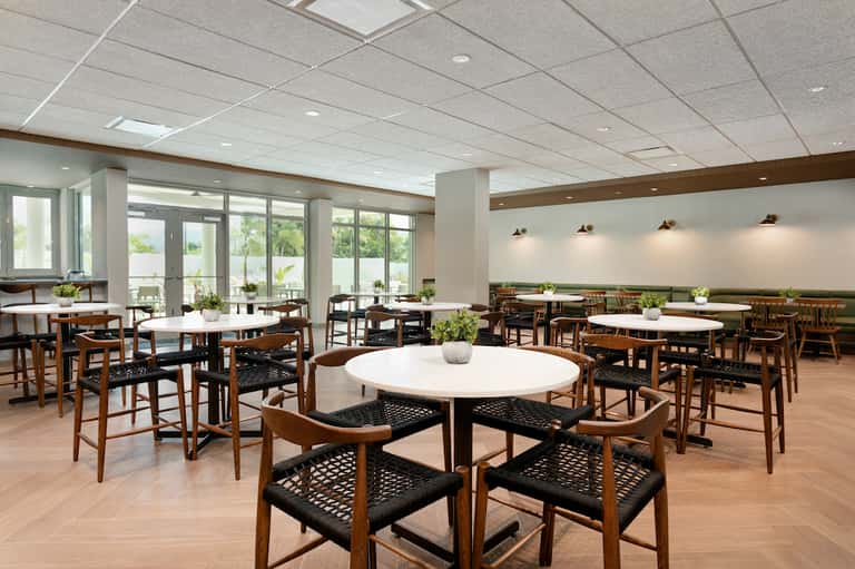 Contemporary dining hall with round white tables, wooden chairs, and wall-to-wall windows