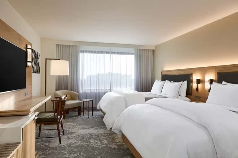 Modern hotel bedroom with two double beds, desk, and balcony with ocean views