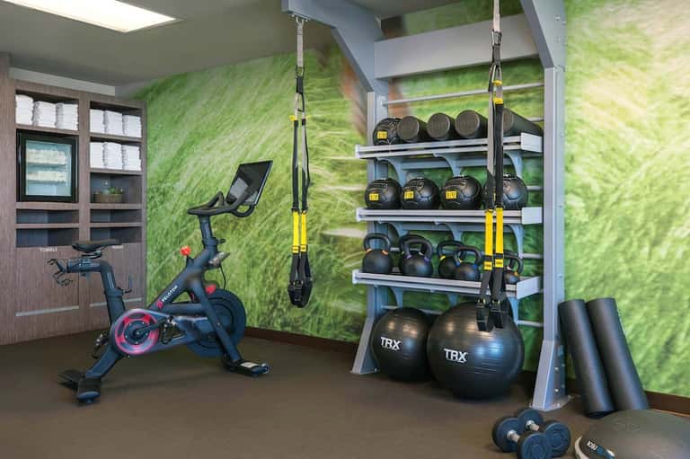 Modern fitness center with exercise bike, TRX suspension equipment, kettlebells, dumbbells, and medicine balls on green wall