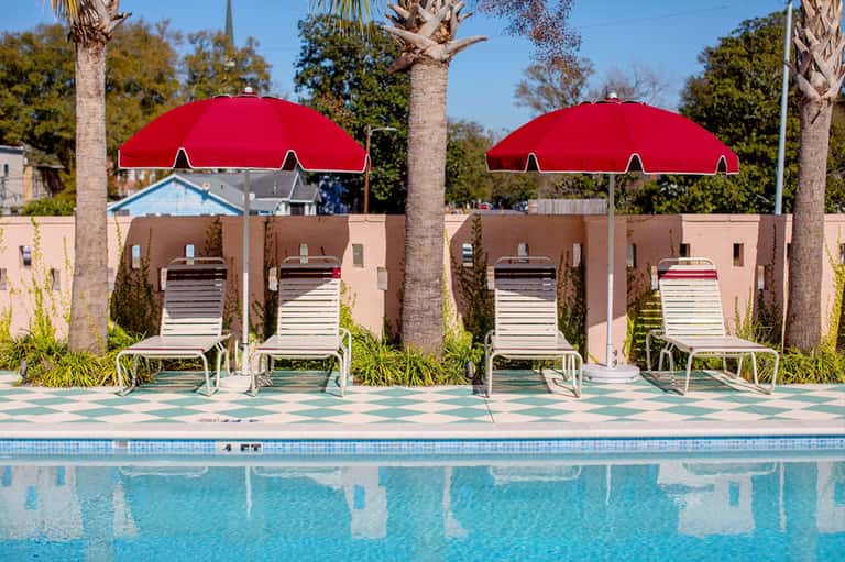 Poolside lounge area with red umbrellas, white loungers, and tan building backdrop