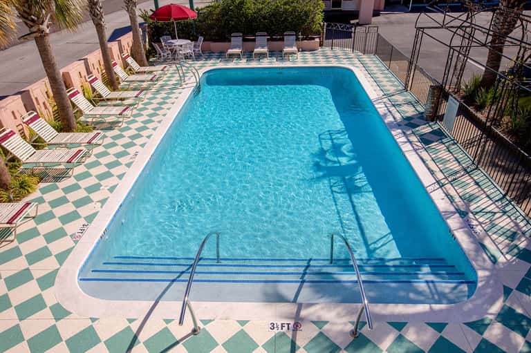 Rectangular lap pool with teal water, checkered deck pattern, and lounge chairs with umbrellas