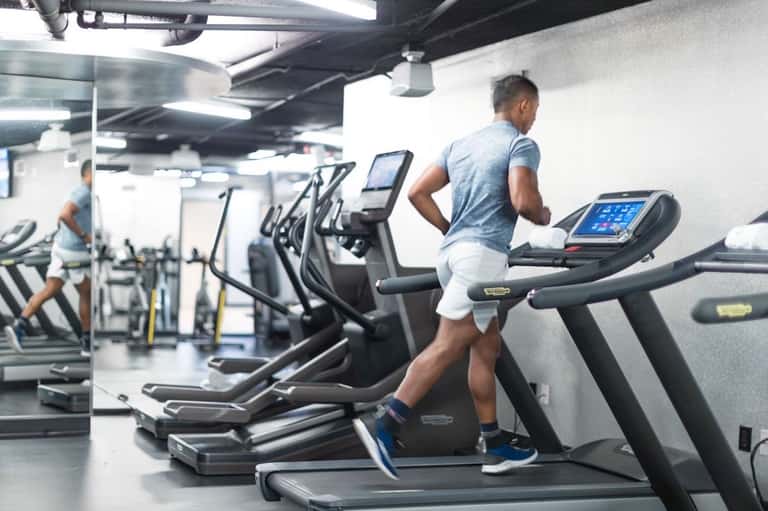 Man running on treadmill in modern gym facility with multiple cardio equipment and bright lighting