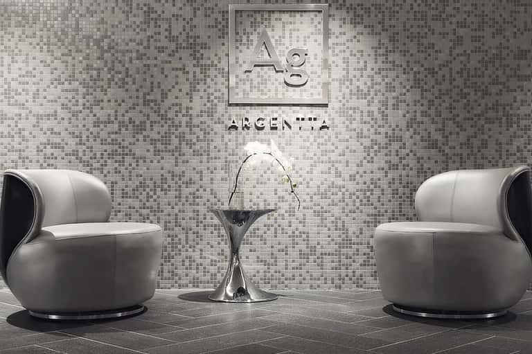Minimalist spa lounge with mosaic tile walls, two modern white armchairs, and small round table