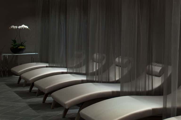Spa relaxation area with curved white lounge seating and sheer gray curtains creating dramatic shadow patterns