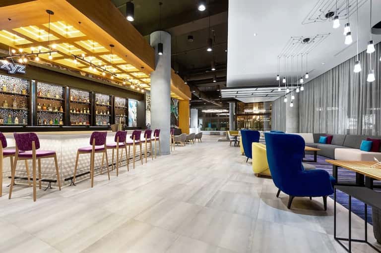 Contemporary hotel lobby and bar area with purple chairs, wooden ceiling, and modern lounge seating