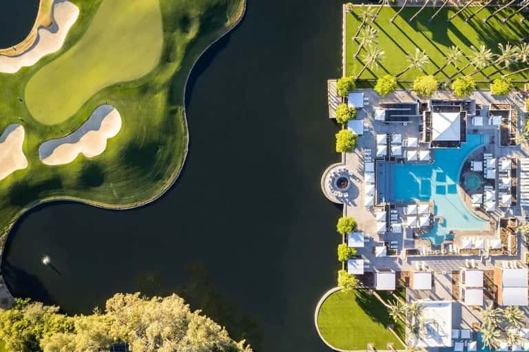 Aerial view of resort with multiple swimming pools, golf course, palm trees, and waterfront location