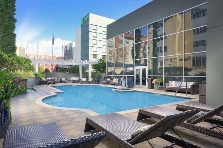 Urban rooftop pool with blue water, lounge chairs, and glass building facade overlooking city