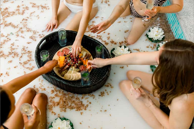 Overhead view of friends sharing a charcuterie platter on a white surface with water lily decorations