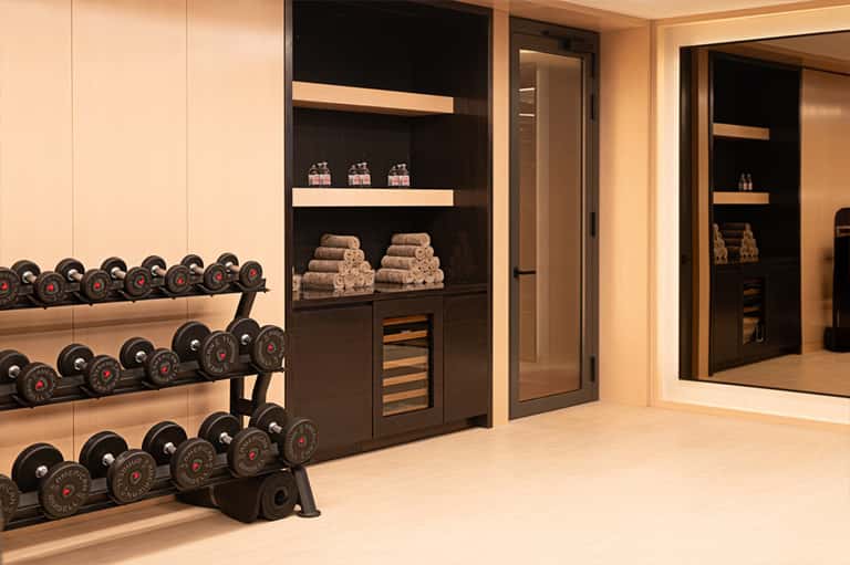 Modern fitness center with dumbbell racks, black shelving units displaying towels, and mirrored walls