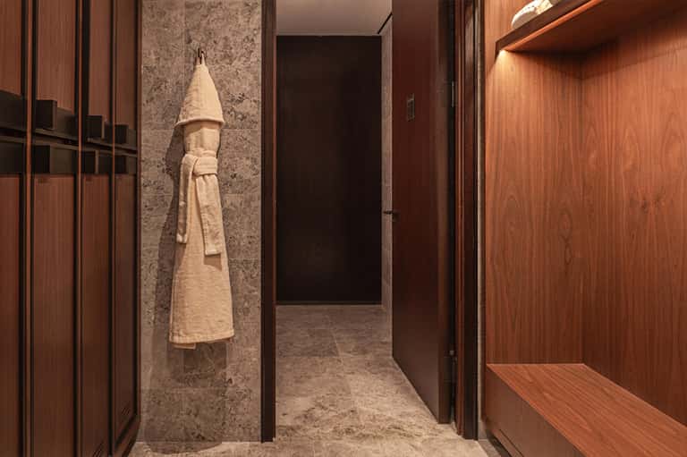 Elegant spa changing room with wood cabinetry, stone walls, and white terrycloth robe